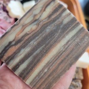 **Alt Text:** A handcrafted bar of Woodland Goat soap from Mother Clucking Farm, made with raw goat’s milk and infused with cedarwood essential oil. The soap is skillfully poured to mimic a wood grain design, offering a bold, earthy fragrance and soothing hydration.